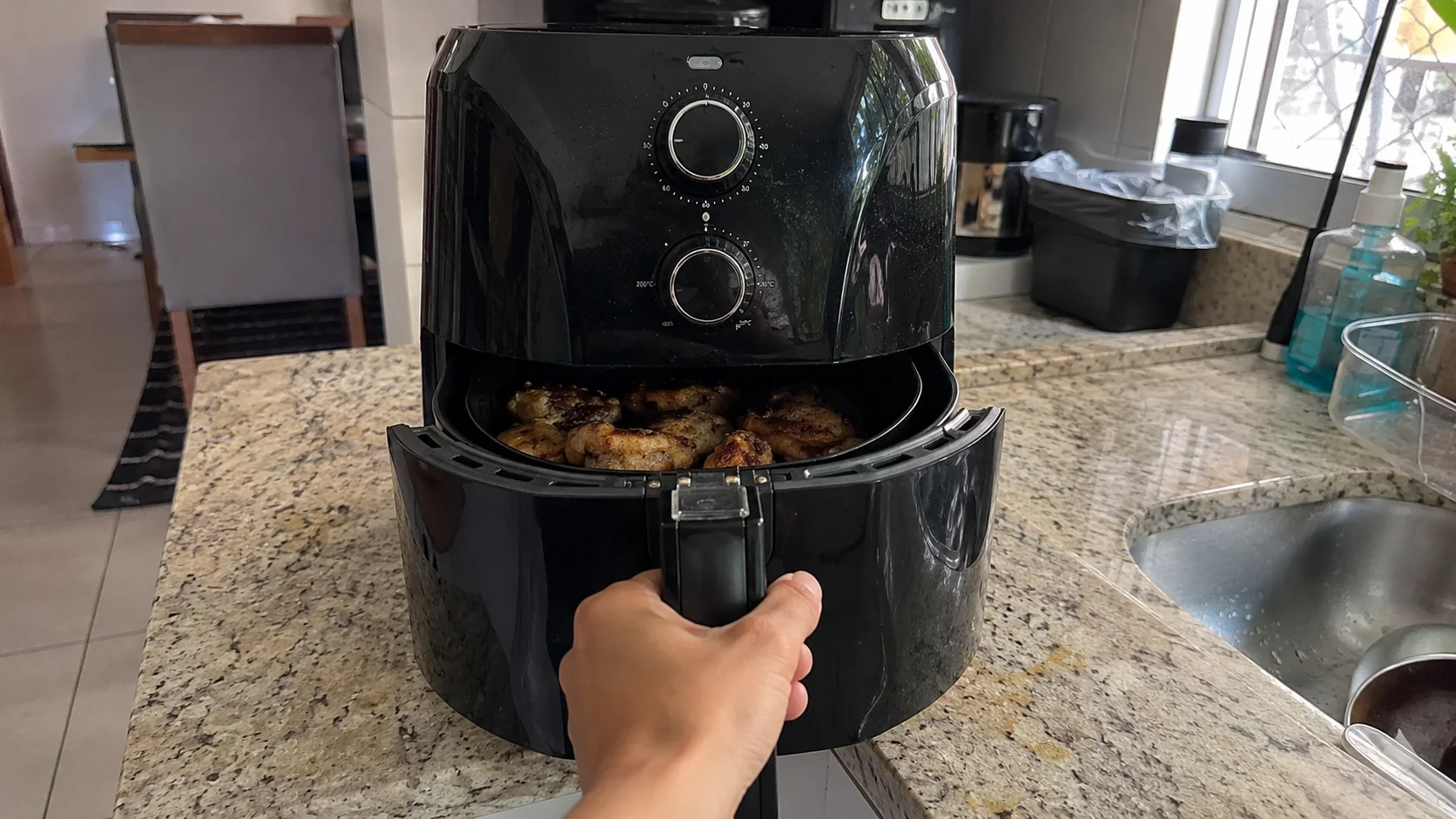 Airfryer Arno Mega AFM7 preta aberta sobre bancada de granito, com mão puxando o cesto e sinais sutis de uso real na cozinha