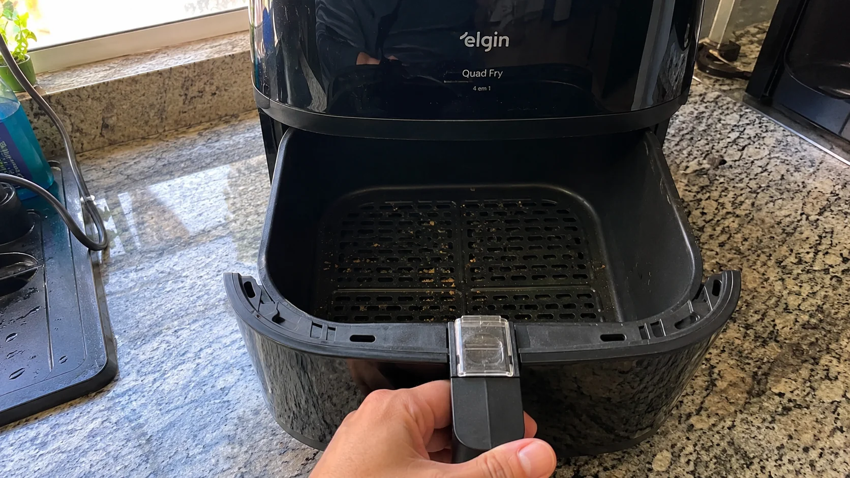 Airfryer Elgin Quad Fry preta aberta sobre bancada de granito, mostrando cesto com leves marcas de uso e mão segurando a gaveta em cozinha residencial